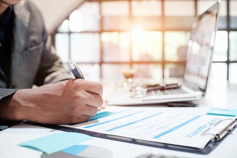 Adult reviewing health insurance documents beside an insurance card and laptop at a kitchen table.